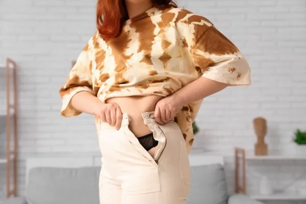 Image of woman trying to do her trousers up after pregnancy weight gain Hounslow