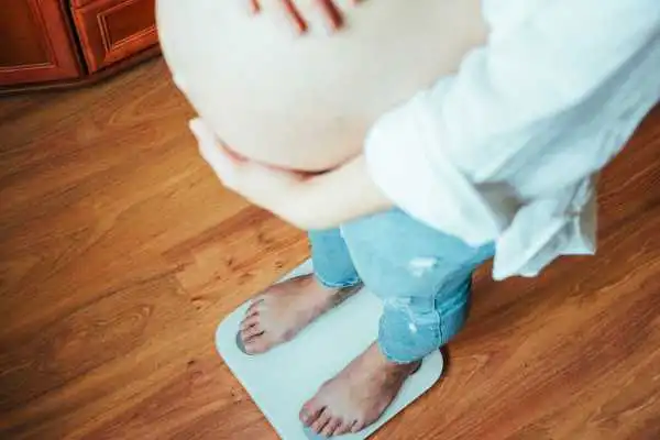 Image of woman weighing herself and experiencing weight gain through pregnancy Hounslow